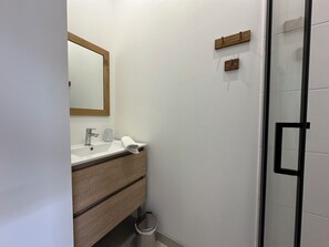 Ett badrum med ett vitt handfat, en spegel, en handduk och en duschkabin med glasväggar.