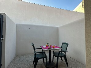 En liten sittplats utomhus med ett bord och två stolar, en krukväxt och en skål med frukt.