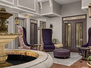 A lobby with a fountain, a purple armchair, and a door with a sign. - La Belle Maison  2-Bedroom Lockoff  Just Steps from the French Quarter (New Orleans)