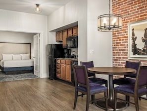 A modern kitchen with wooden cabinets, a dining area with a round table and purple chairs, and a brick accent wall. - La Belle Maison  2-Bedroom Lockoff  Just Steps from the French Quarter (New Orleans)