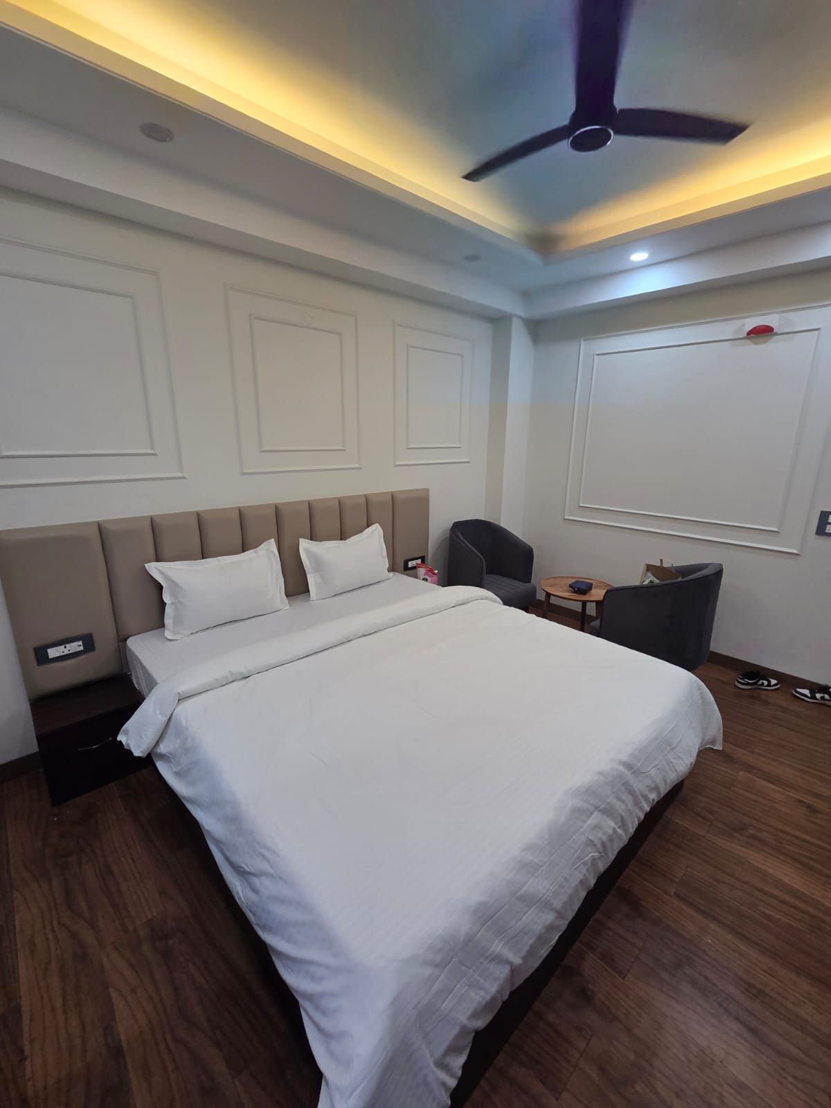 Une chambre d’hôtel avec un grand lit, un ventilateur de plafond, un bureau avec une chaise et une petite table.
