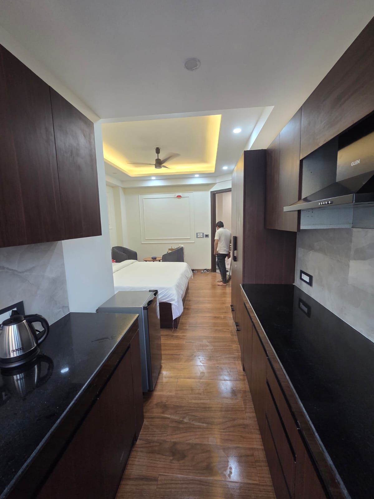 Une chambre d’hôtel compacte comprenant un coin cuisine, un lit, un ventilateur de plafond et une petite table.