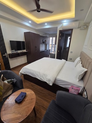 Una habitación de hotel con una cama, televisor, escritorio y ventilador de techo.