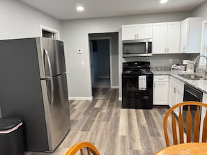 Cozinha moderna com eletrodomésticos de aço inoxidável, armários brancos e piso de madeira em padrão herringbone.