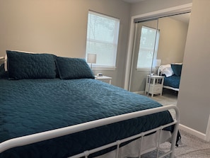 Quarto com cama, mesa de cabeceira, espelho e janela com persianas.