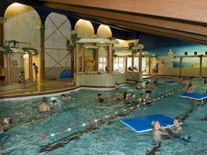 Una piscina interior con varias pistas, una zona de juegos infantiles y una zona de estar cubierta.