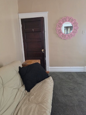 Une pièce avec un canapé beige, une porte sombre, une petite table en bois et un miroir décoratif rose accroché au mur.