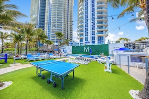 Un área de piscina con mesa de ping pong, sillones de descanso y un tablero de ajedrez.