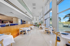 Een modern restaurant met een lange toonbank, meerdere tafels en grote ramen met uitzicht op het omliggende landschap.