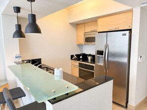 Una cocina moderna con isla de vidrio, electrodomésticos de acero inoxidable e iluminación colgante.