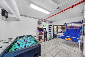Una habitación con mesa de fútbol de mesa, juegos de arcade y una silla azul con balones de baloncesto.