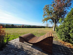 Una boscada de fusta en un camp herbós, amb un arbre i un cel serè al fons.
