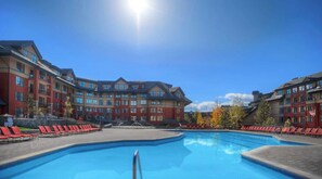 Ein Hotel mit Schwimmbad, roten Liegestühlen und blauem Himmel.