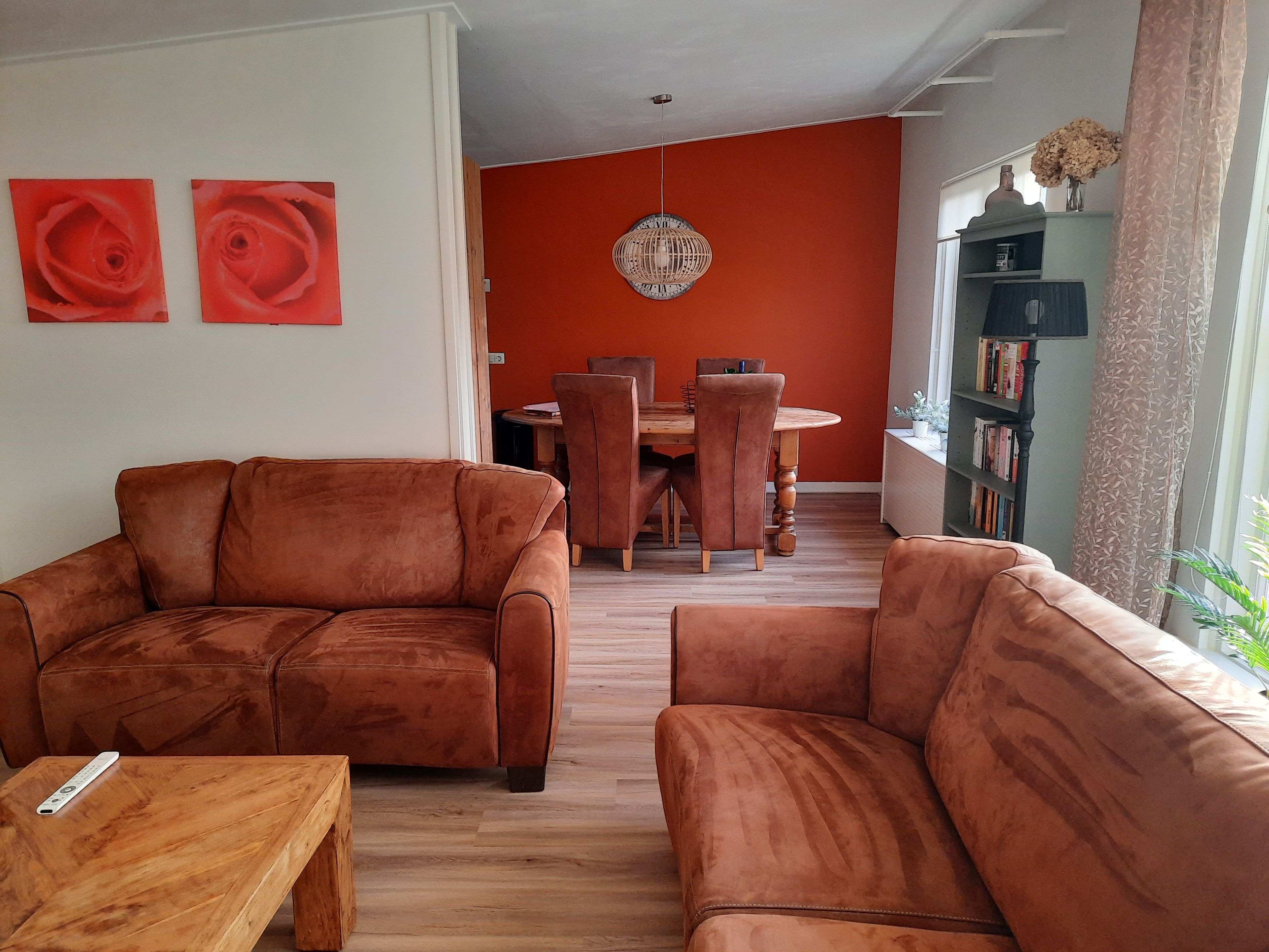 Een woonkamer met twee bruine banken, een houten salontafel en een eethoek met een ronde tafel en stoelen.