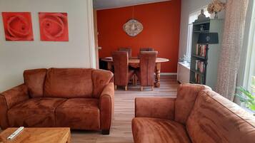 Een woonkamer met twee bruine banken, een houten salontafel en een eethoek met een ronde tafel en stoelen.