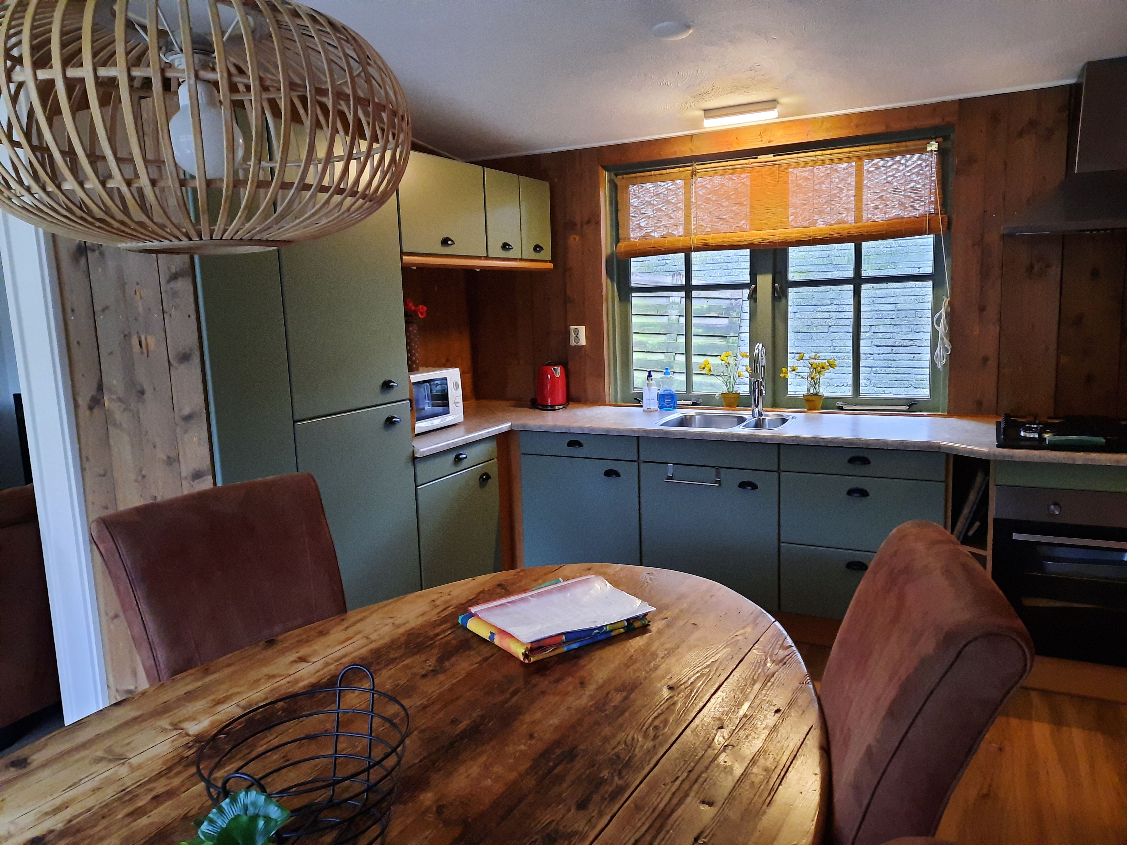 Una cocina con armarios de madera, microondas, lavamanos y una mesa de comedor con sillas.
