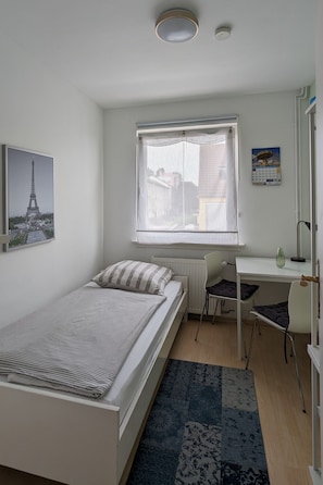Een slaapkamer met een bed, een bureau, een stoel, een radiator, een raam met gordijnen, een kalender en een foto van de Eiffeltoren.