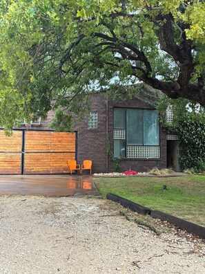 Una casa moderna con fachada de ladrillo, un ventanal grande y un árbol en primer plano.