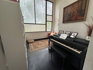 Una habitación con un piano, un tapete, una ventana con vistas y un cuadro en la pared.
