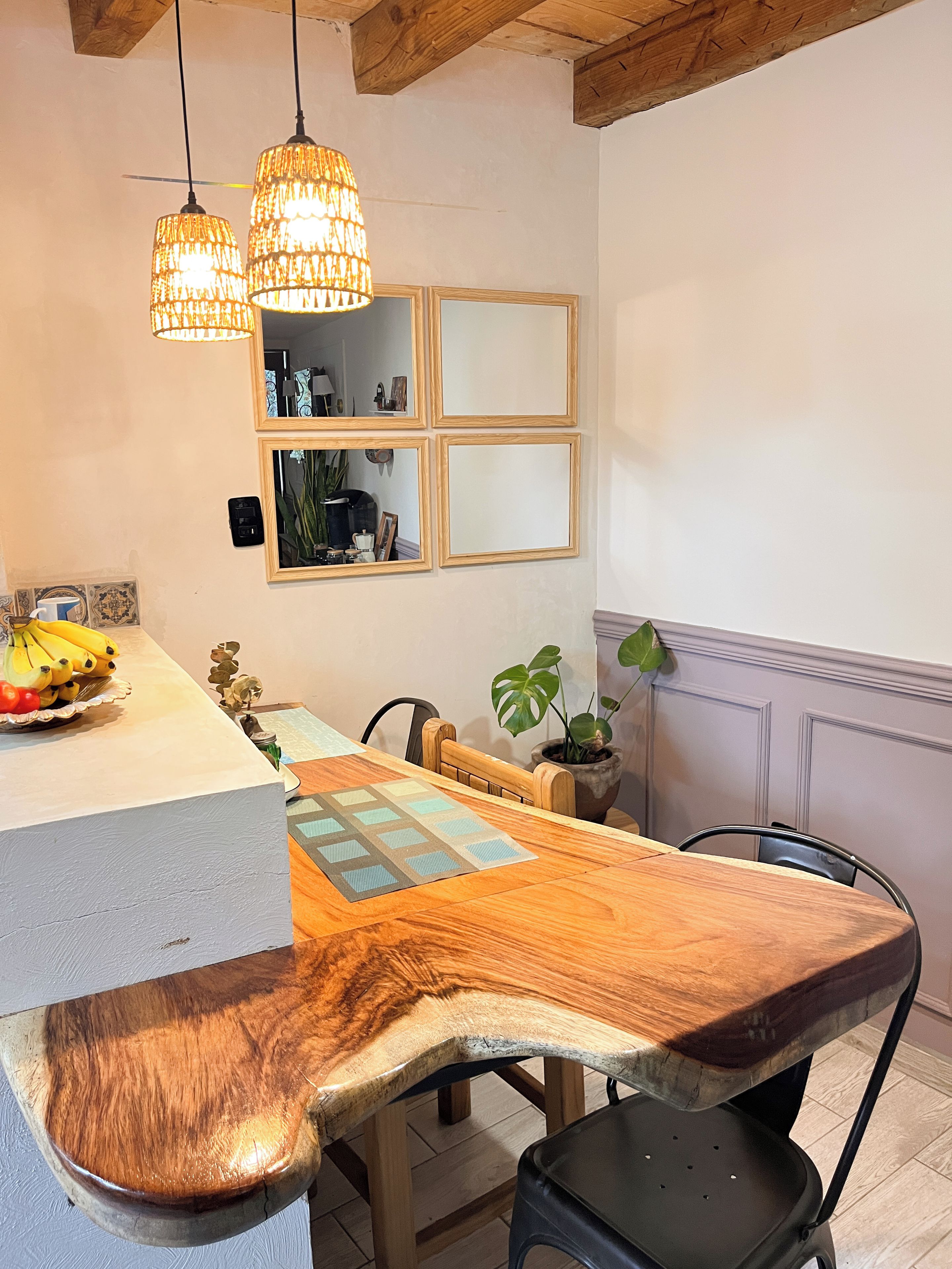 Ein Essbereich mit Holztisch, Stühlen, hängenden Pendelleuchten und einem an der Wand befestigten Spiegel.