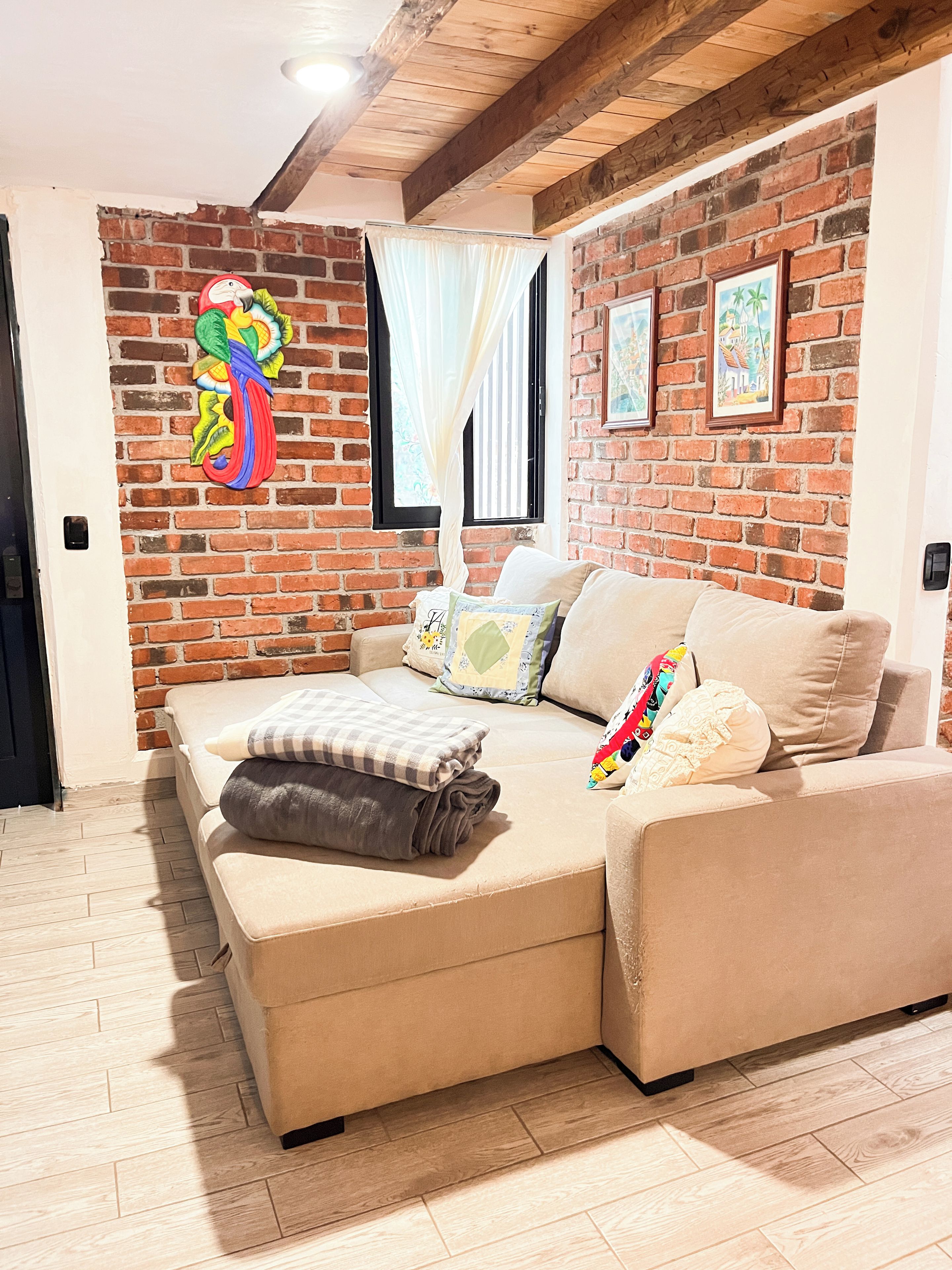 Un salon chaleureux avec un mur en briques, un canapé et un élément de décoration murale aux couleurs vives.