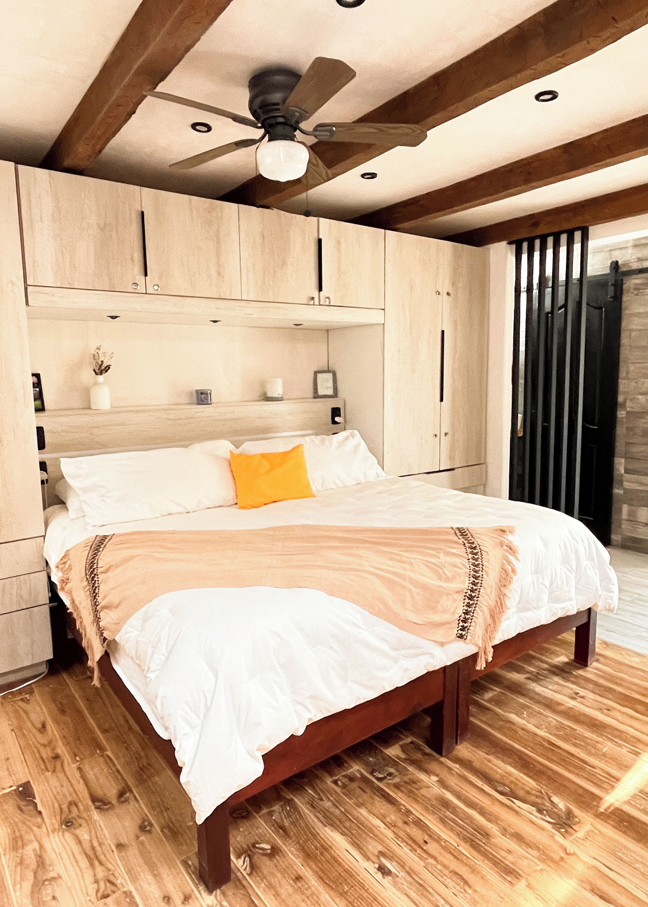 Une chambre avec un lit en bois, un ventilateur de plafond et une armoire en bois.