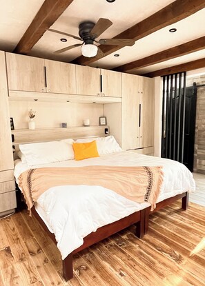 Une chambre avec un lit en bois, un ventilateur de plafond et une armoire en bois.