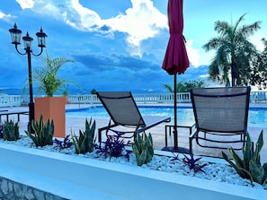 A poolside area with lounge chairs, a lamp post, and a view of the sea. - Stunning Oceanview 2BR-Pool-Balcony & 24/7 Security (Montego Bay)