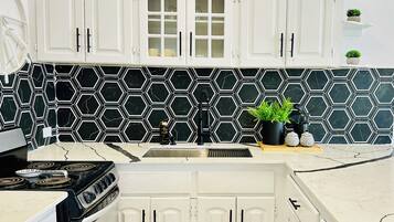 A kitchen with white cabinets, a black and white hexagonal backsplash, a stove, and a sink.
