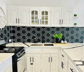 A kitchen with white cabinets, a black and white hexagonal backsplash, a stove, and a sink. - Stunning Oceanview 2BR-Pool-Balcony & 24/7 Security (Montego Bay)