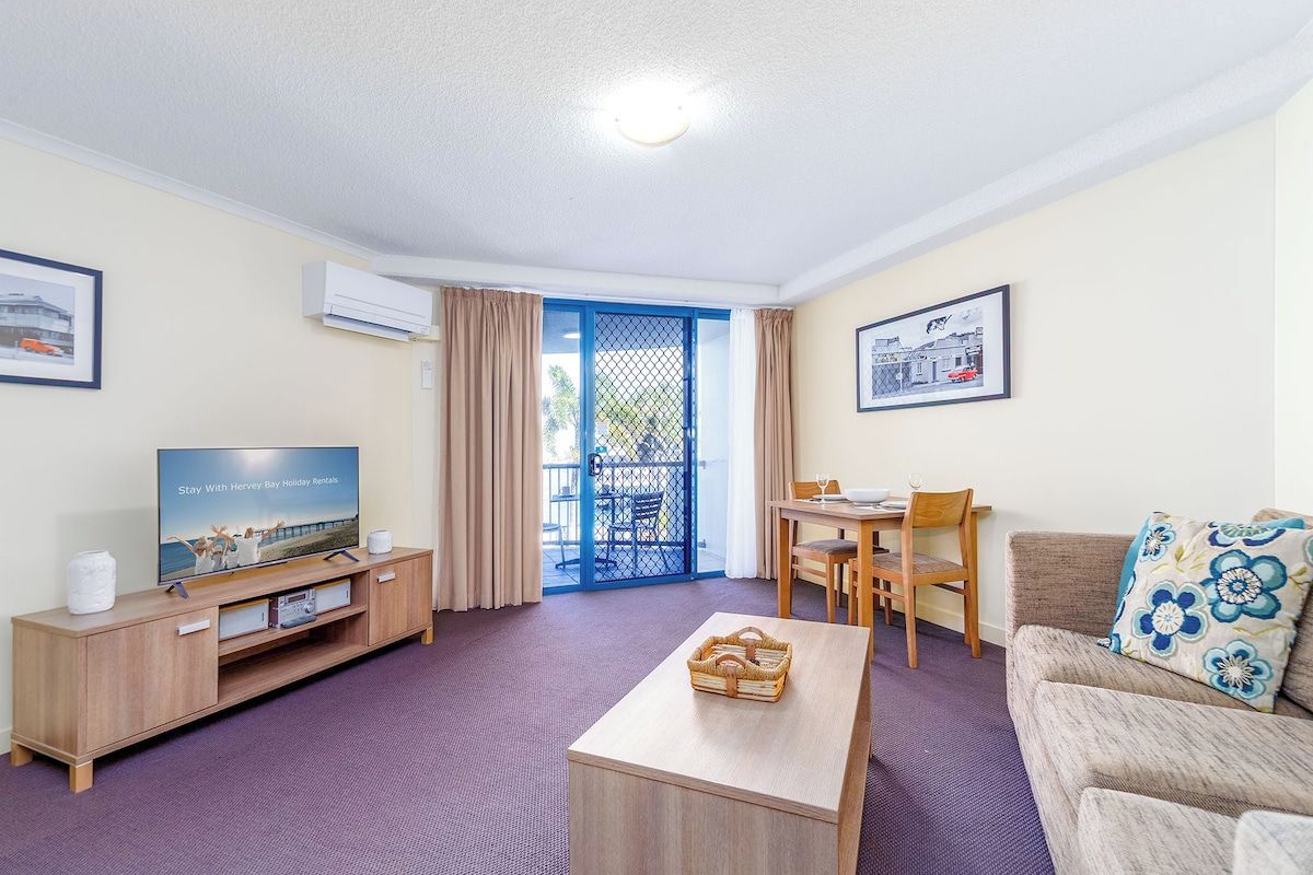 A furnished living room with a television, a dining table, and a sofa.