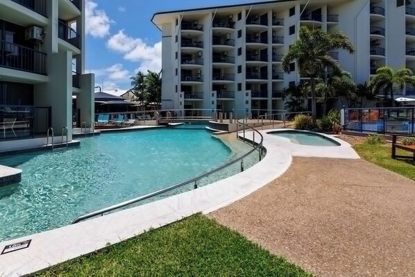 A hotel pool area with multiple swimming pools, a covered seating area, and a building with balconies. - Mantra Apt - 2nd Floor + Views (Urangan)