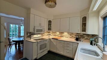 A kitchen with white cabinets, a microwave, a stove, and a sink. There is a dining table with chairs and a chandelier.