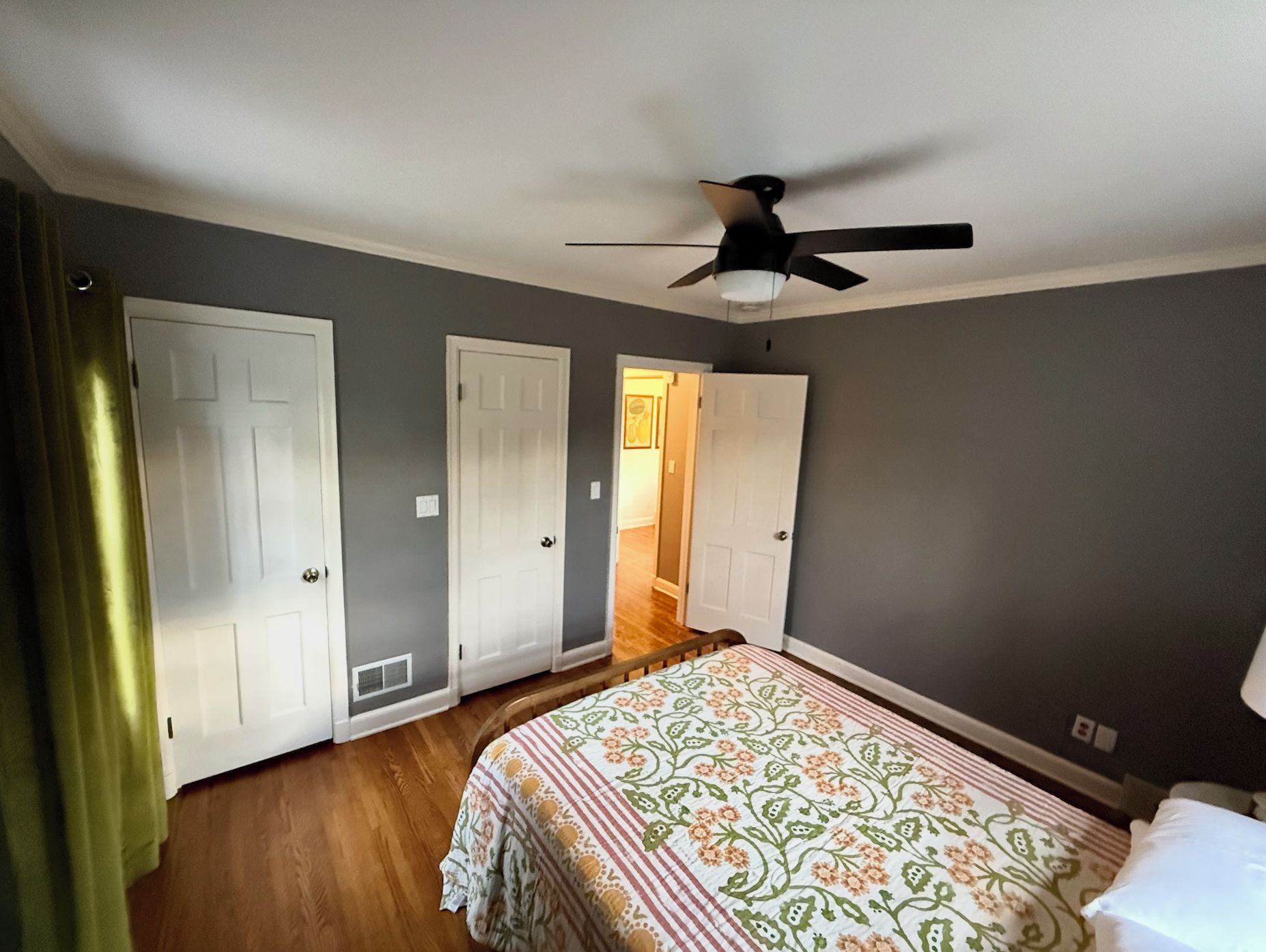 A bedroom with a bed, a ceiling fan, and three white doors.