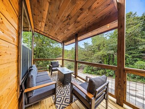 A wooden deck with a sofa and table, surrounded by glass walls offering a view of greenery. - Indoor Pool • Arcade • Hot Tub  Pigeon Forge (Pigeon Forge)
