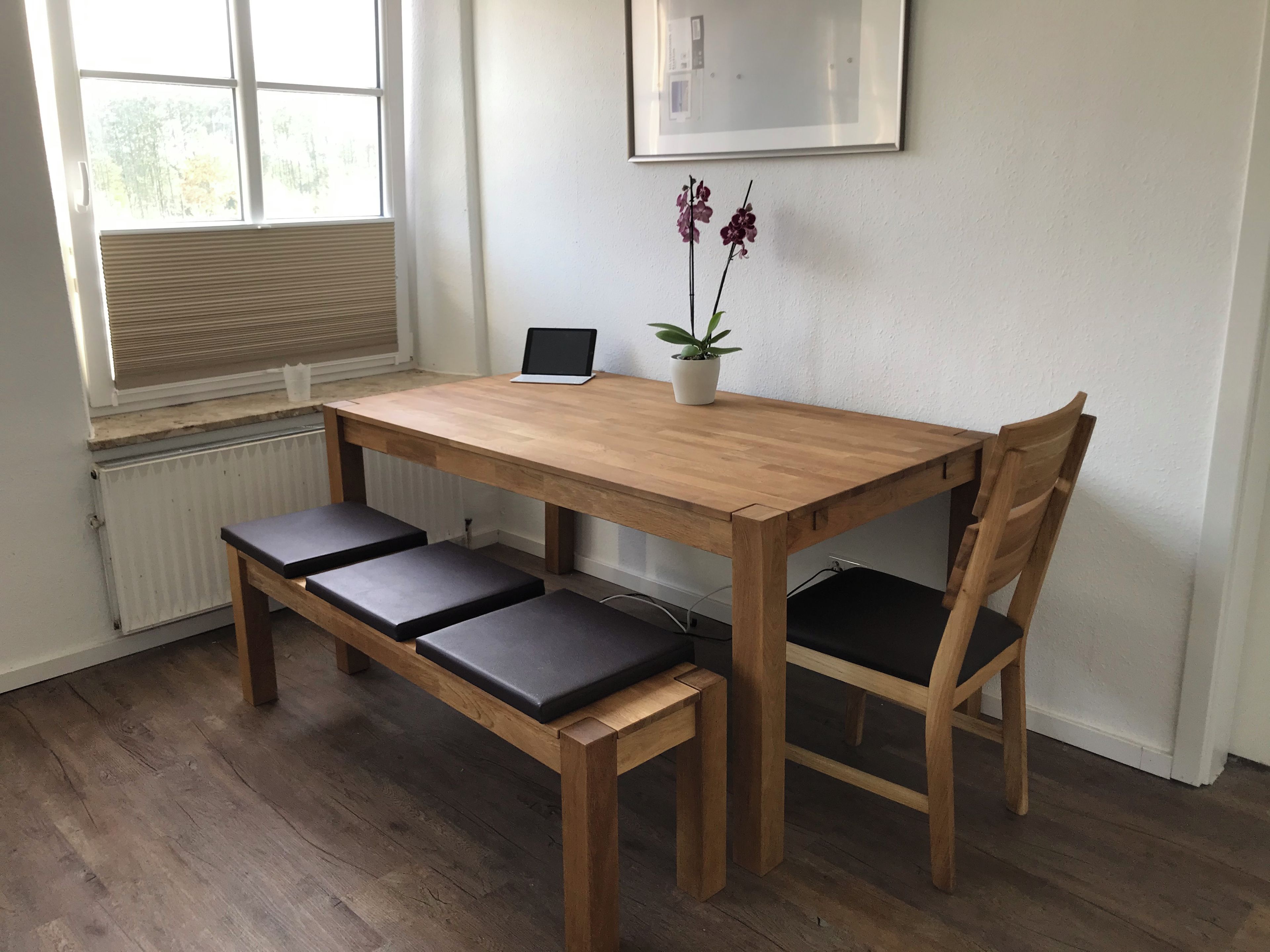 A wooden dining table with a laptop and a potted plant on it.