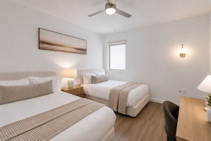Een hotelkamer met twee bedden, een plafondventilator, een raam en een nachtkastje met een lamp.
