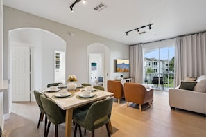 A spacious living area with a dining table, chairs, and a sofa. There is a balcony with a view of the outside. - Palm Haven- Spacious 3BR Condo in Windsor Palms Resort (Kissimmee)