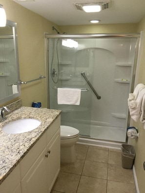 Un baño con lavamanos de encimera de granito, inodoro, ducha con mampara de vidrio y espejo.