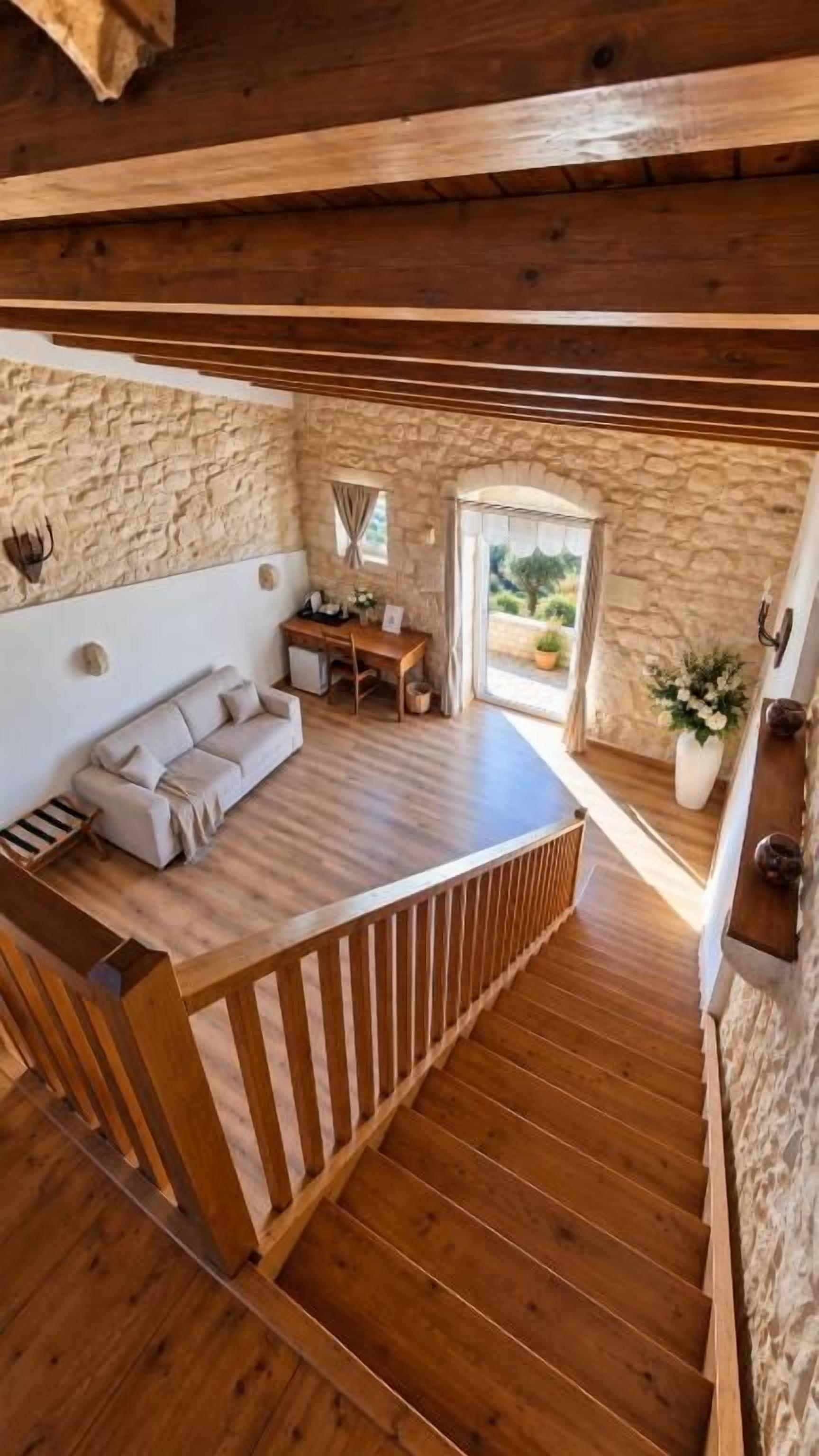 Una escalera de madera que conduce a un dormitorio en el entrepiso, con una pared de piedra, un sofá y un escritorio.