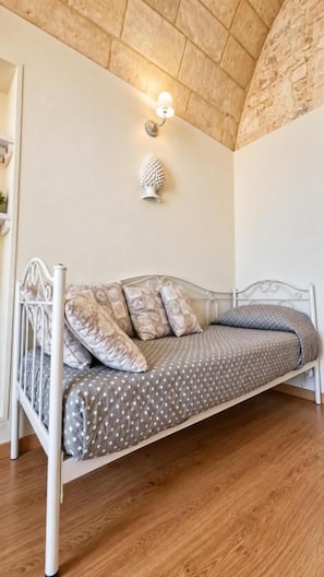 Een enkel bed met een metalen frame en beddengoed met een patroon in een kamer met houten vloer en een stenen plafond.
