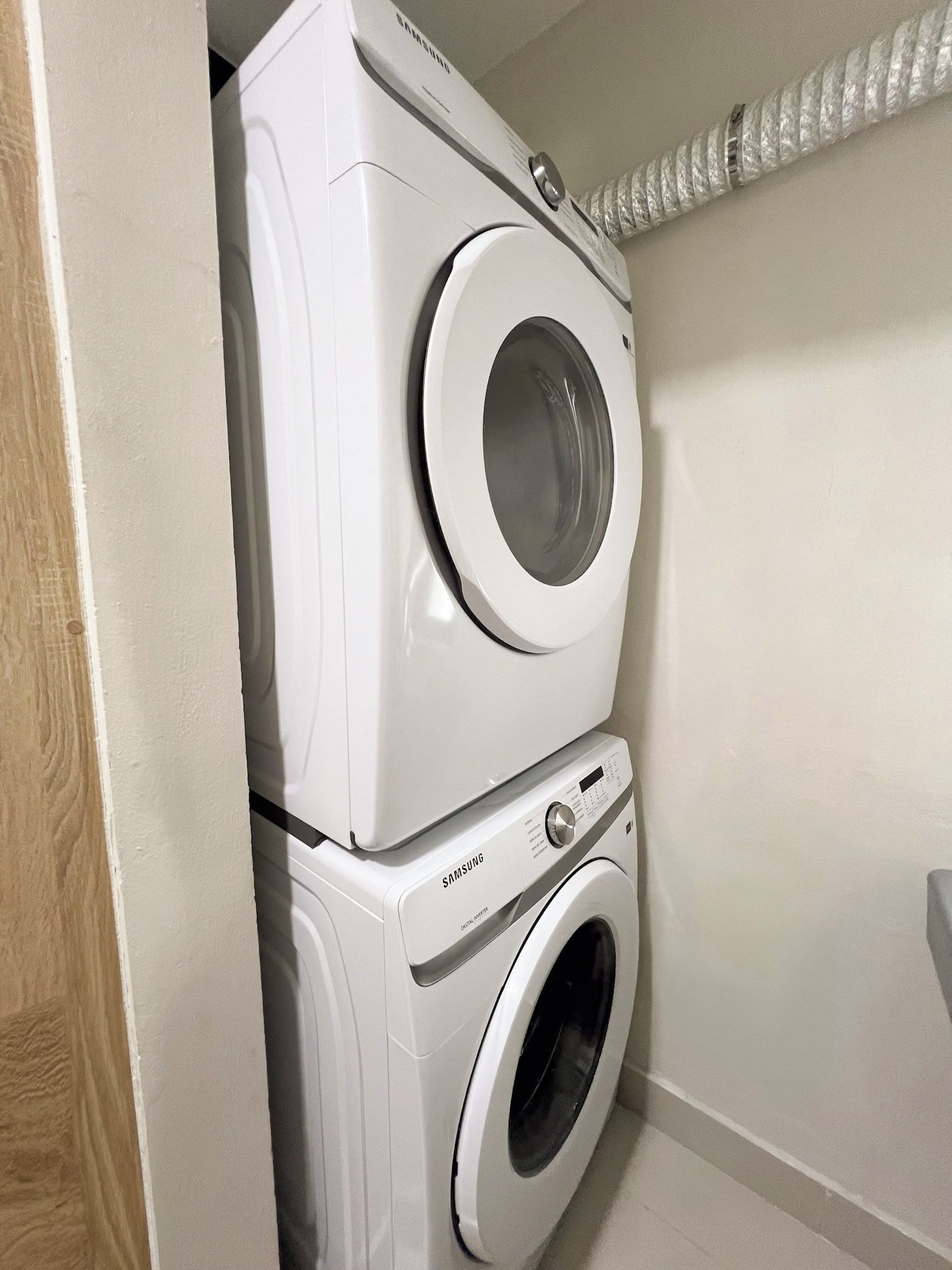 A stacked washer and dryer unit in a corner with a white wall and a wooden door frame.