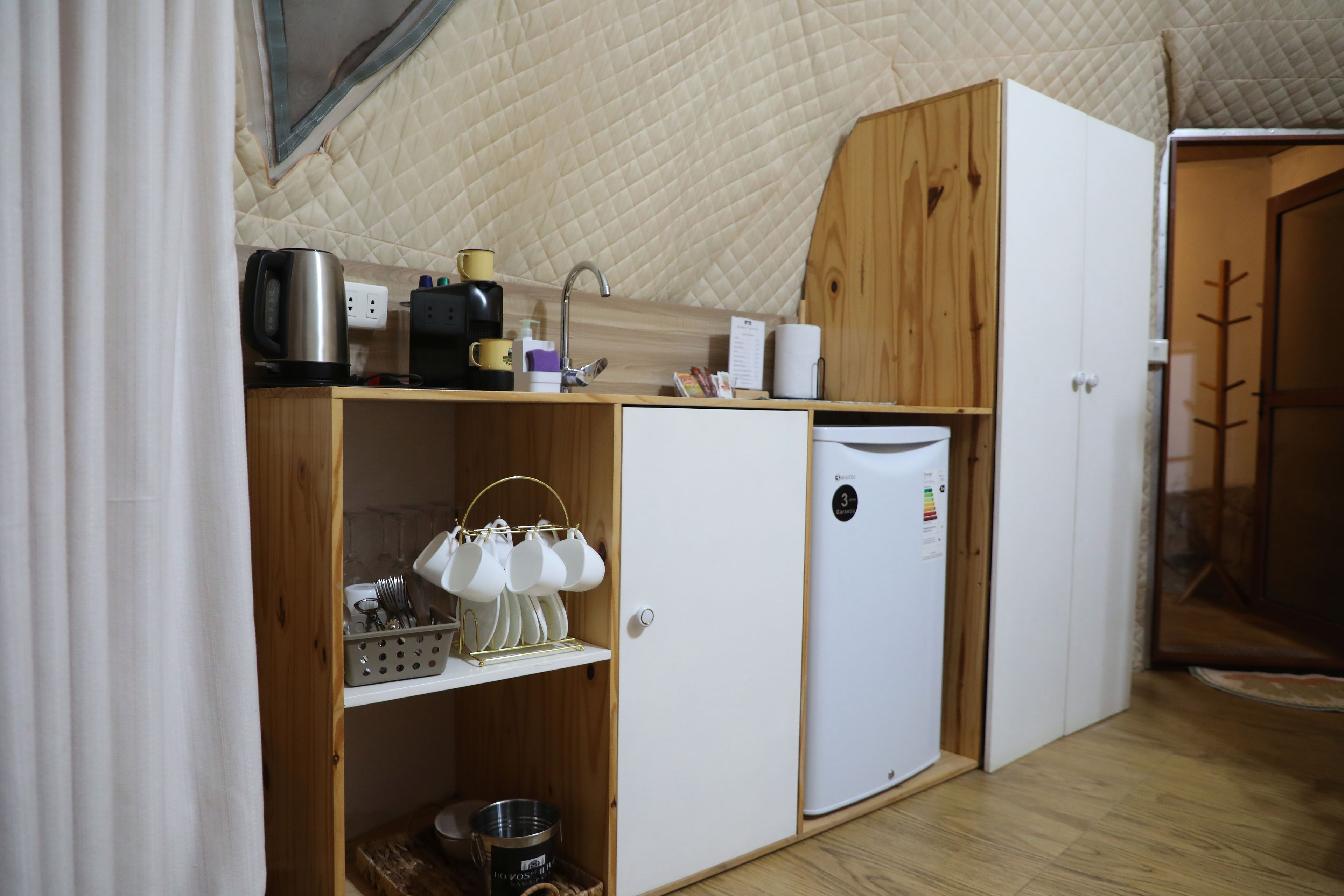 Una kitchenette compacta con cafetera, hervidor y un refrigerador pequeño.