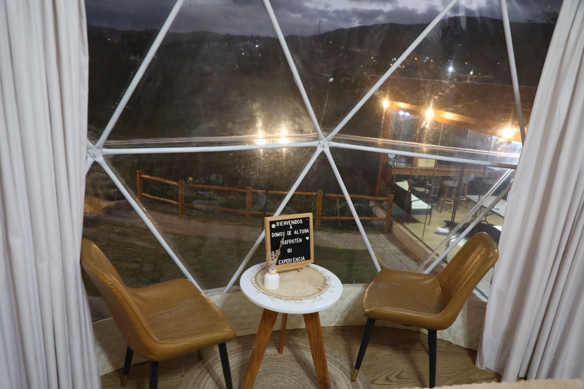 A room with a glass dome structure, two chairs, a small table, and a welcome sign.