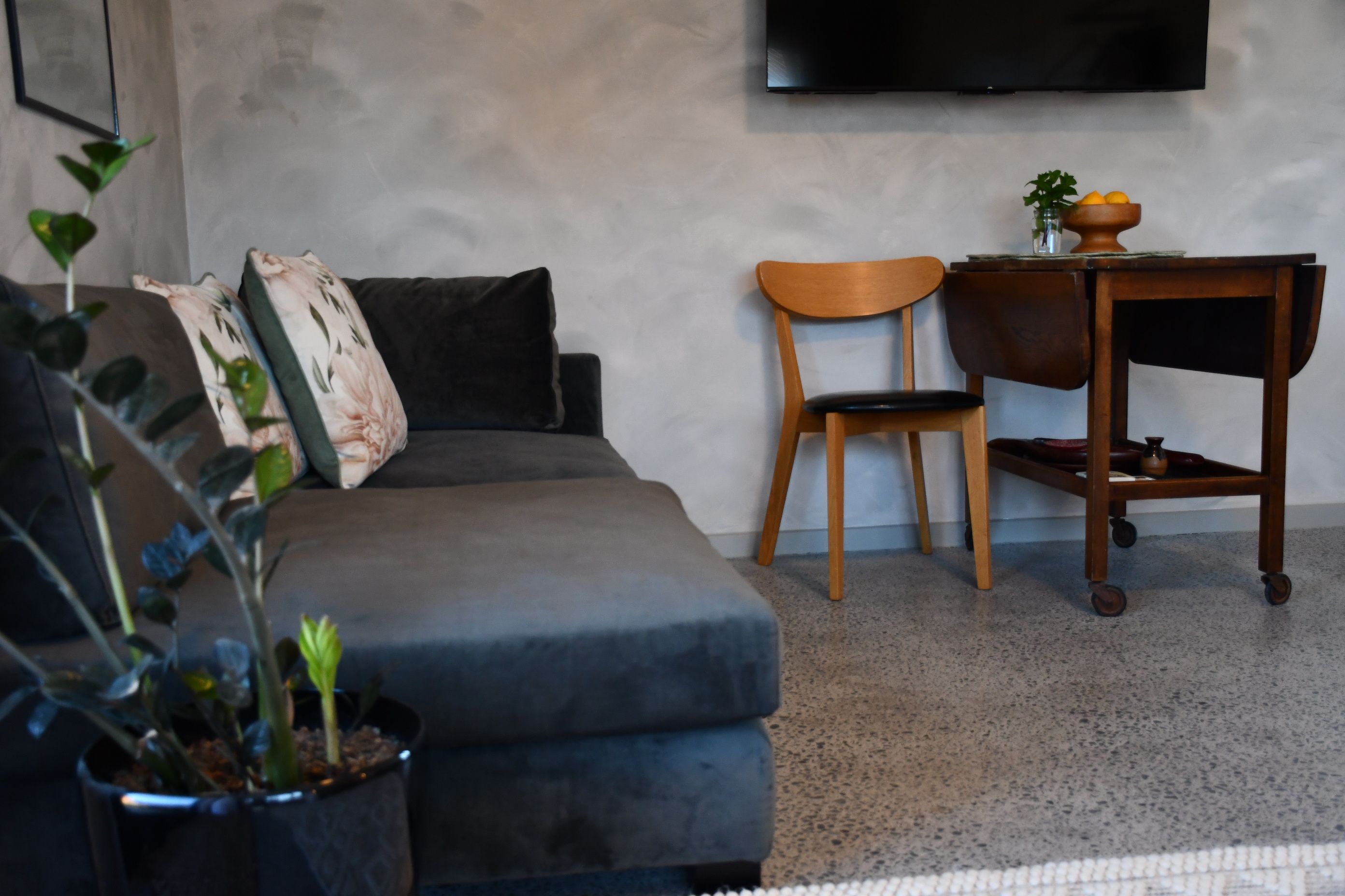 A living room with a grey sofa, a wooden chair, a small table with a vase, and a potted plant.