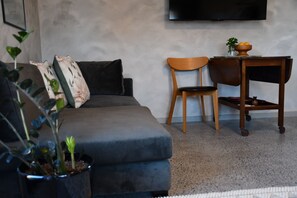 Een woonkamer met een grijze bank, een houten stoel, een bijzettafeltje met een vaas en een kamerplant.