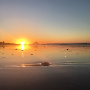 Een strand met de ondergaande zon aan de horizon, wat een rustige en vredige sfeer creëert.