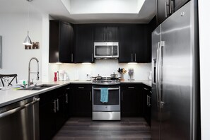 Une cuisine moderne avec des meubles de couleur sombre, des appareils en acier inoxydable et un îlot central doté d’un évier et d’un plan de travail.