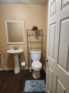 A bathroom with a pedestal sink, toilet, and a metal shelf with a vase. - The Southern Spot (Baton Rouge)