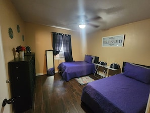 Une chambre avec deux lits, une commode, un miroir, un ventilateur de plafond et un panneau décoratif mural.